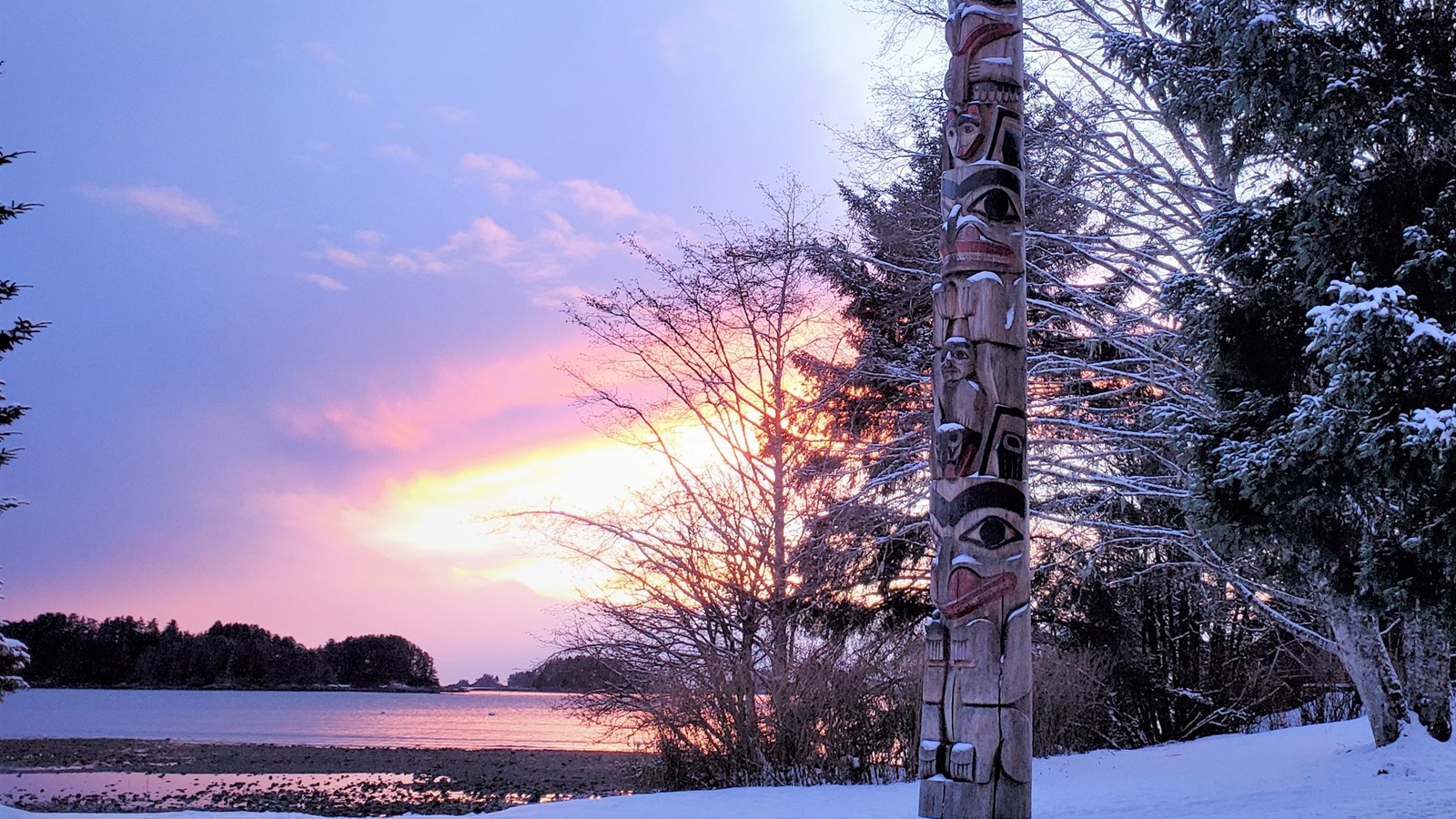 A Totem Pole overlooking the ocean during a sunset on a winter evening.
