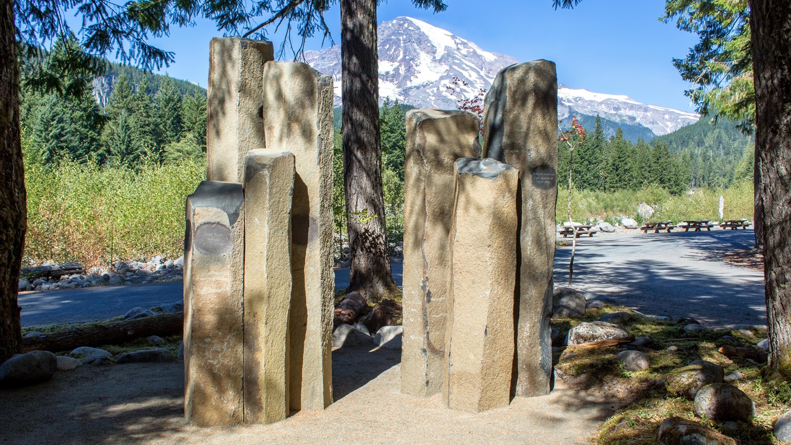 A cluster of columnar rocks arranged upright in front of a view of Mount Rainier. 