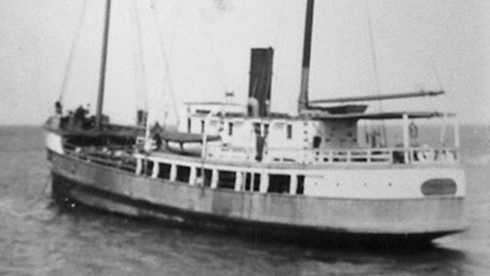 Large boat with two masts and smoke stack in middle 