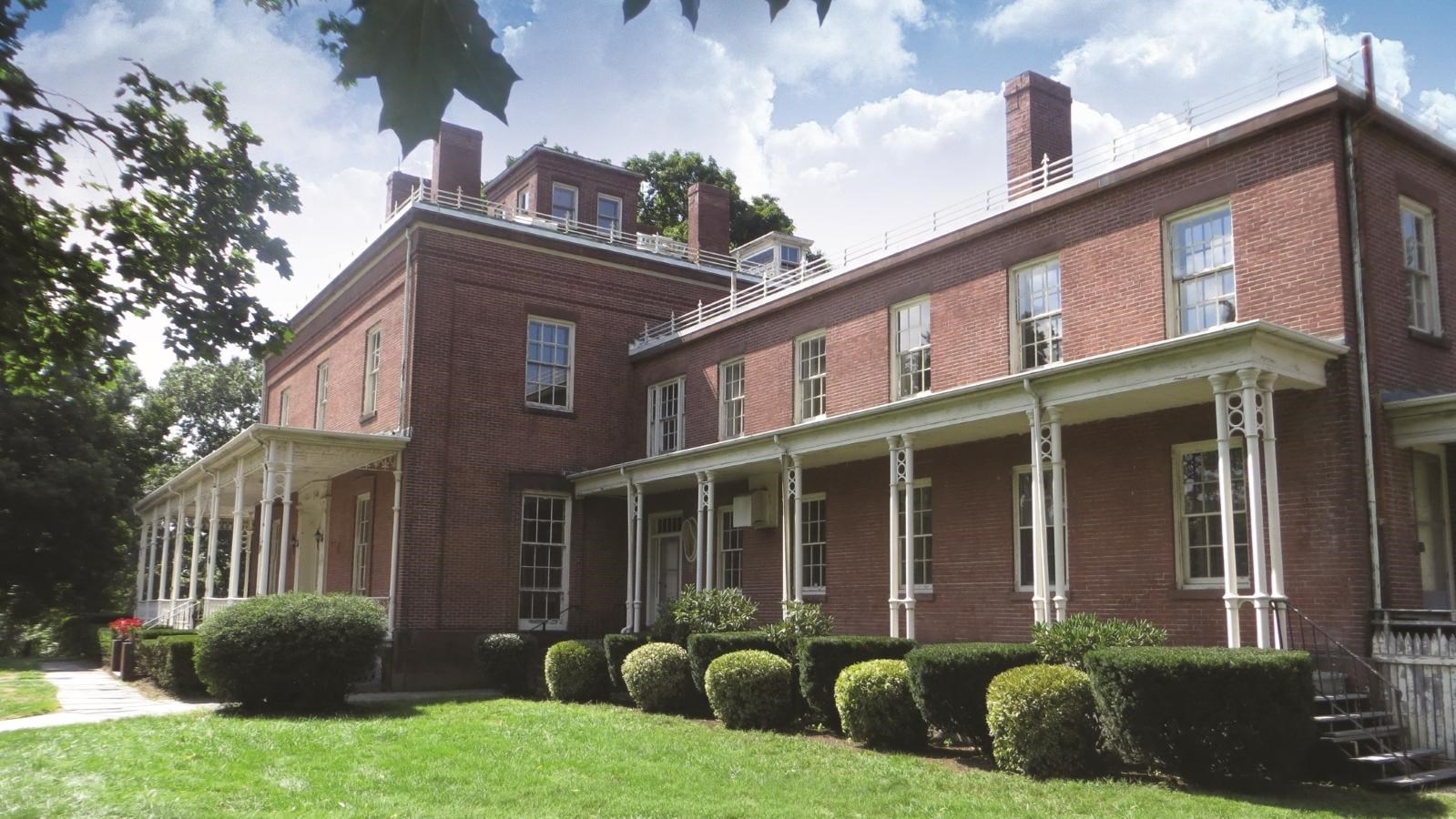 A red brick building with shrubs in front of a deck on a sunny summer day..