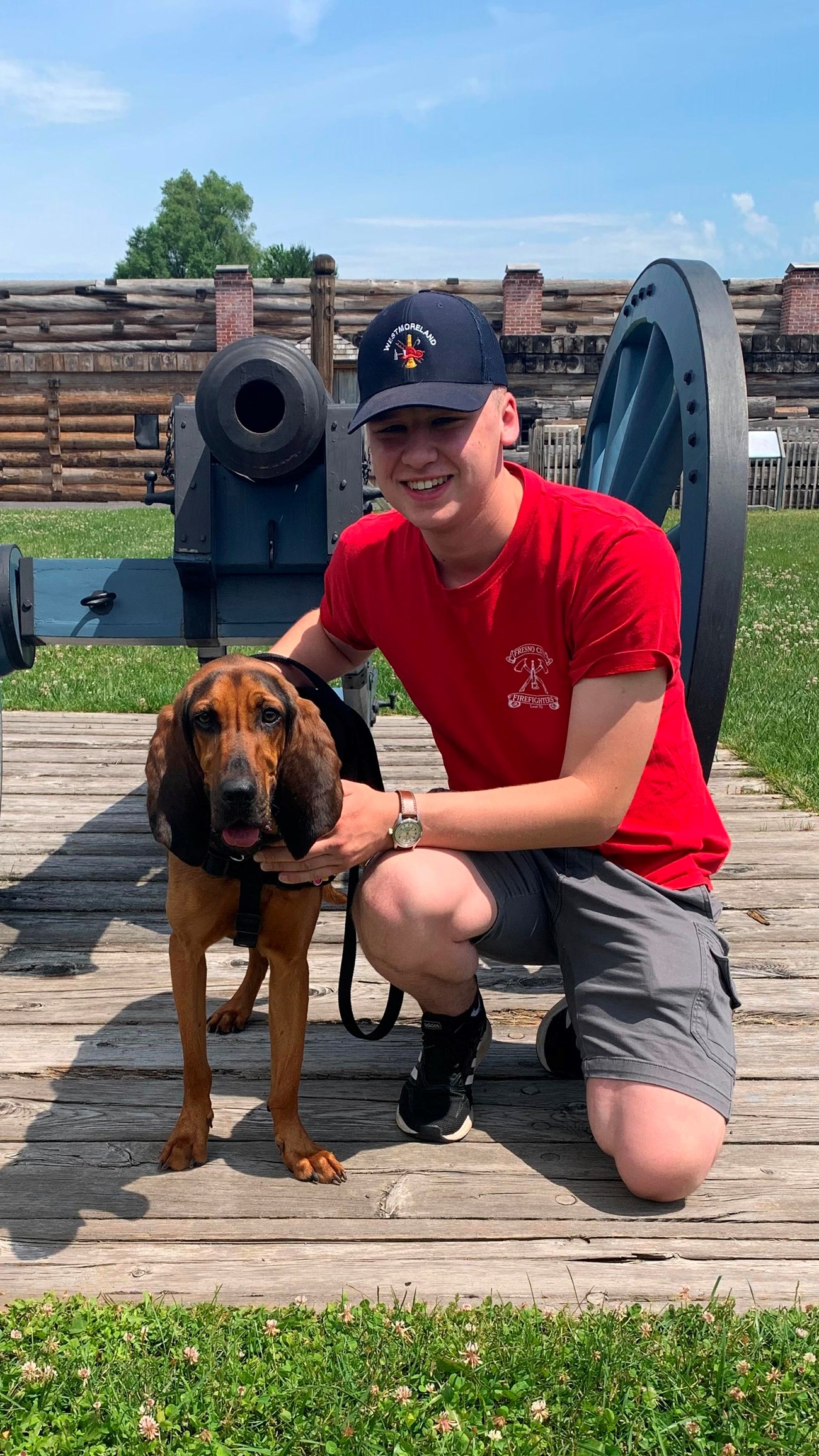 A sweet doggy stands on a leash with his person in front of a cannon.