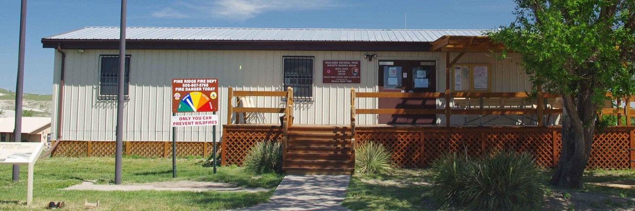 a squat tan building with a brown porch and a tree.