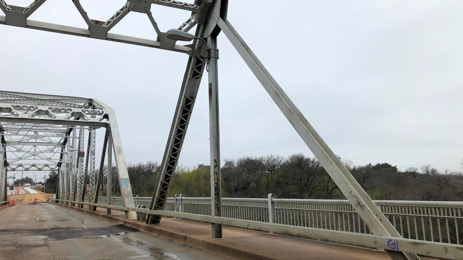 Standing under the metal trusses of a large bridge, looking out towards a city.