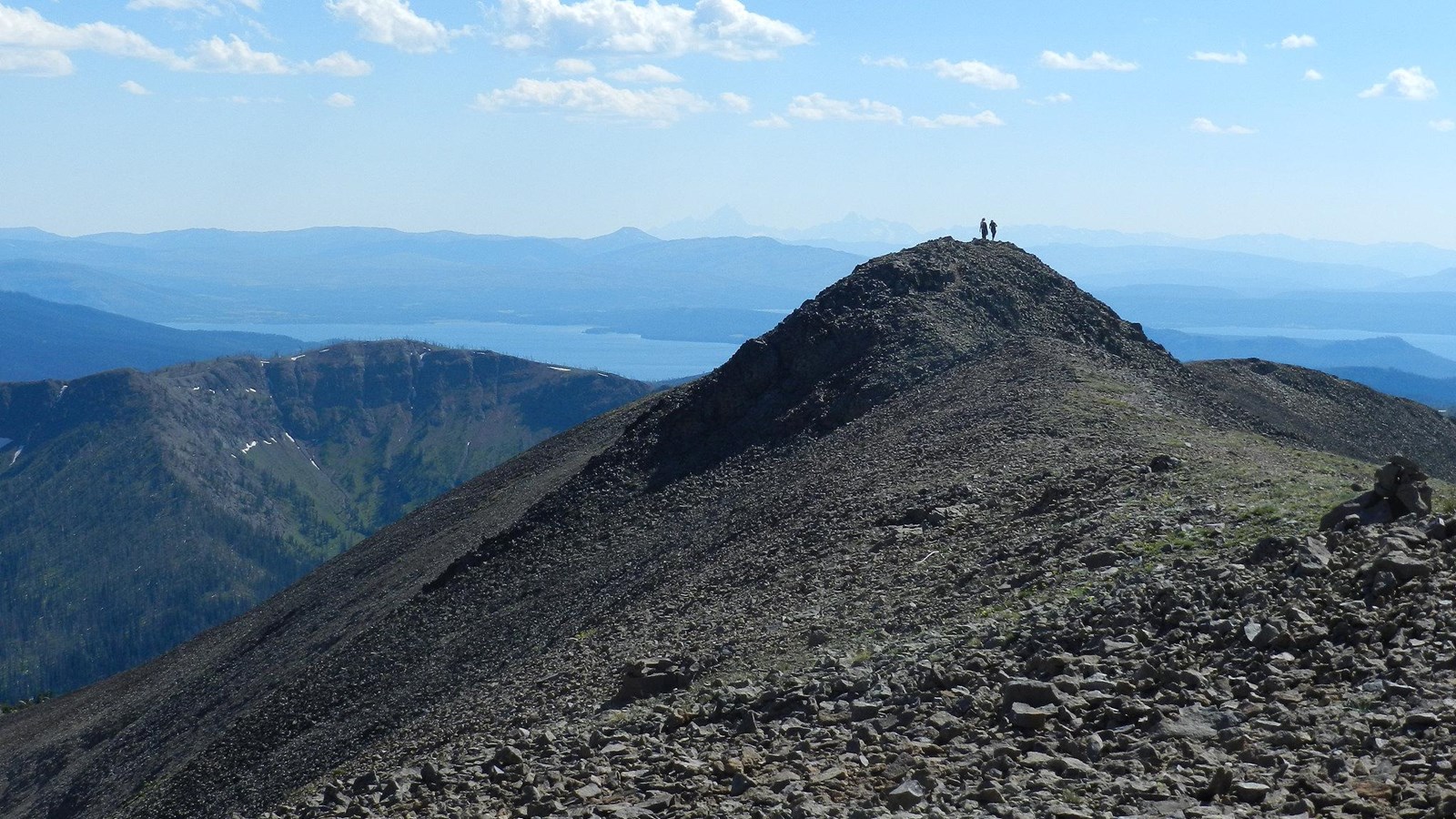 Two hikers enjoying the view of mountains in the distance from the summit of rocky mountain.