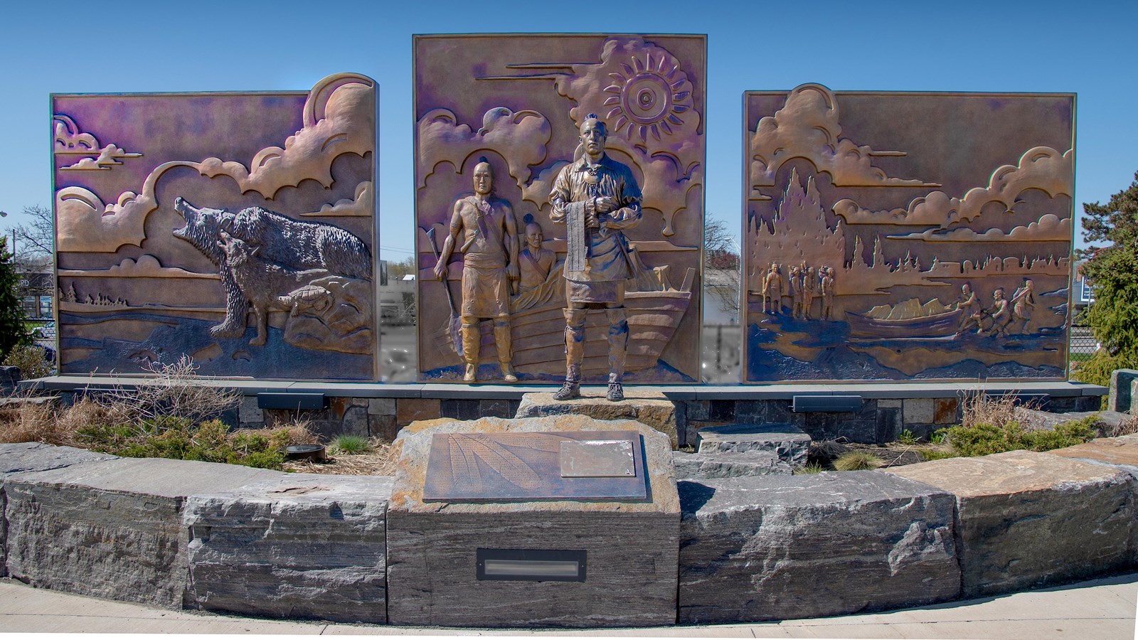 Three large, shiny bronze panels depict different scenes of early Native and European relations.