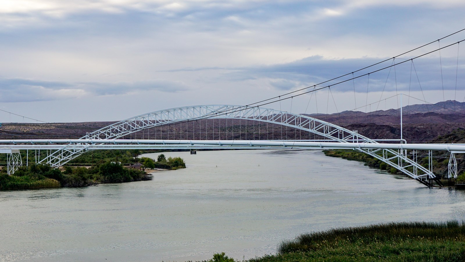 A large white metal bridge spanning a river, with two arches that parallel each other.