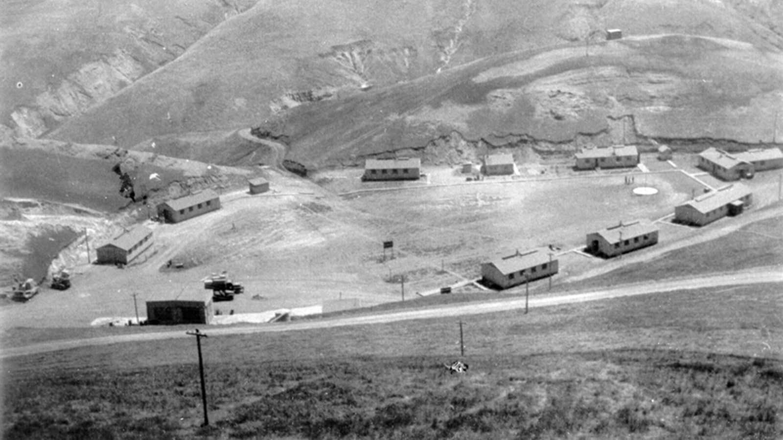 Series of small buildings on the edge of a flat grassy area.