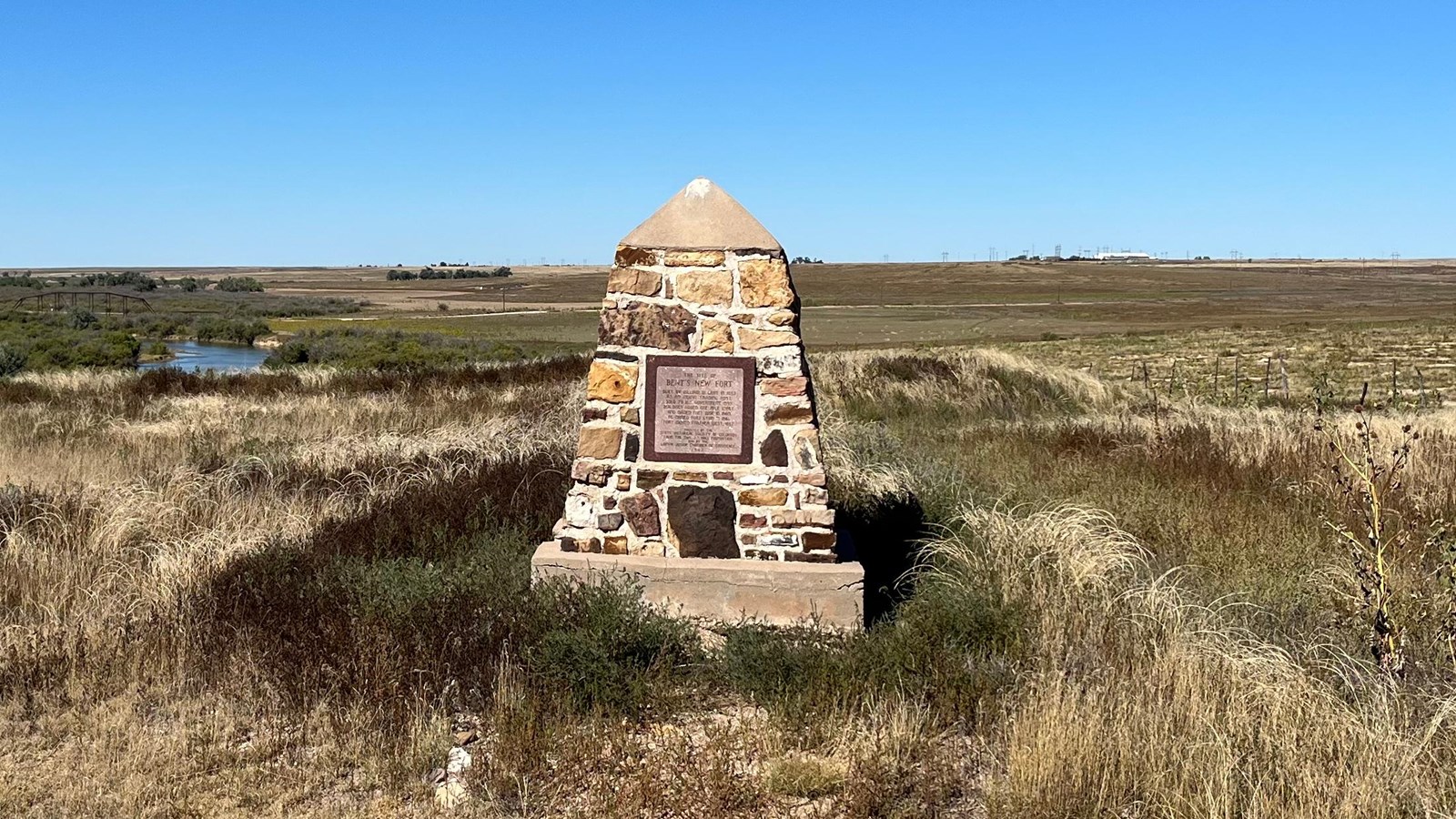 Stone monument rises above a prairie landscape and blue sky. 