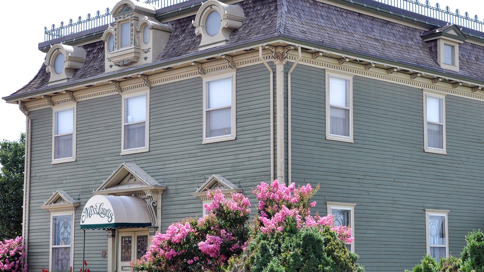 Pale green  two and half story vistorian mansion with pale mustard yellow trim.