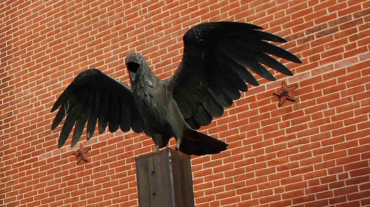 A statue of a raven sitting atop a plinth stands outside a three story brick house.