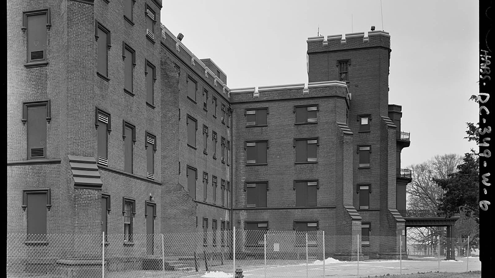 A four story brick building with boarded up windows behind a chain link fence.