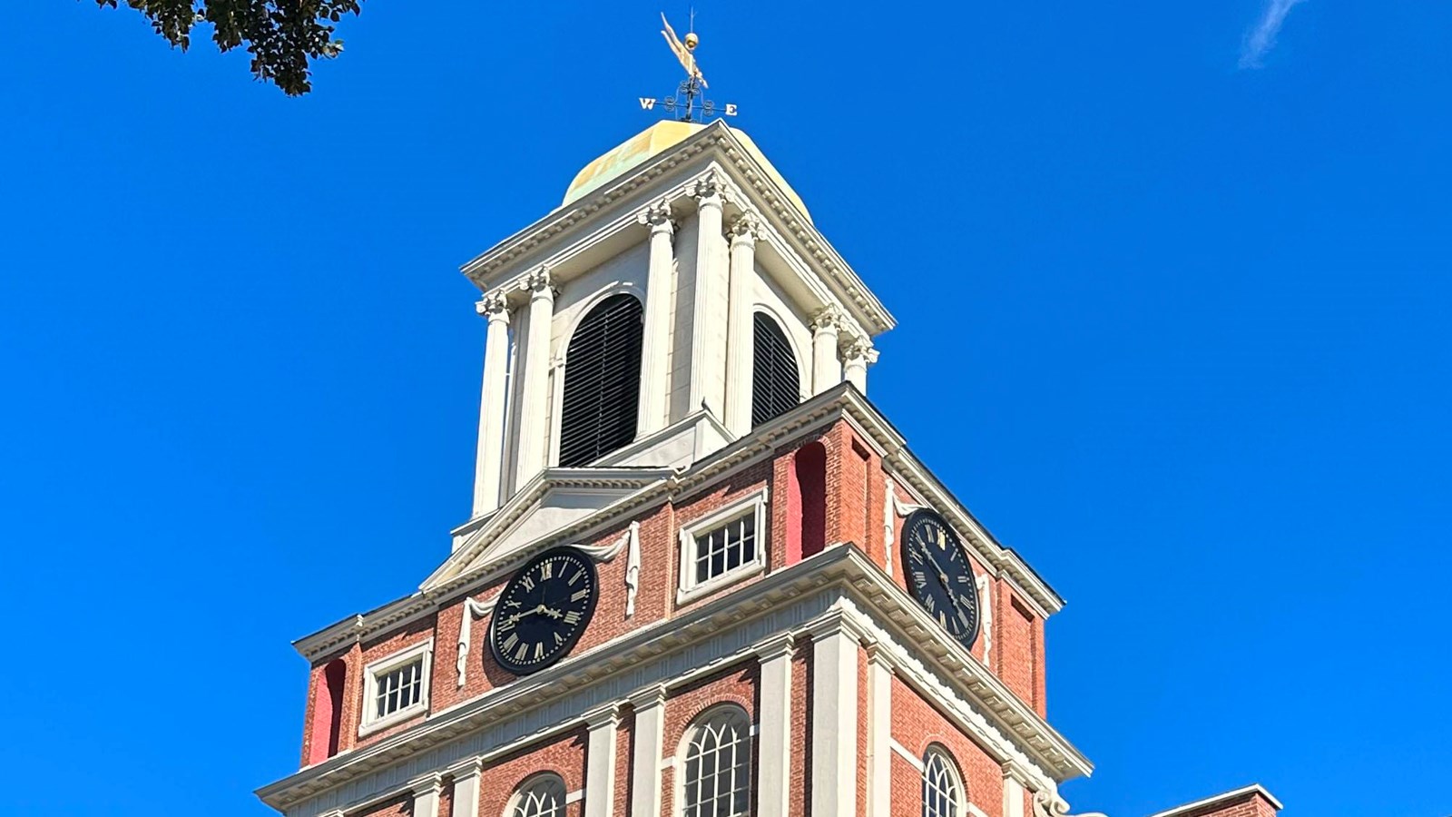 View looking up at the church, built out of brick it has a square front and a white bell tower