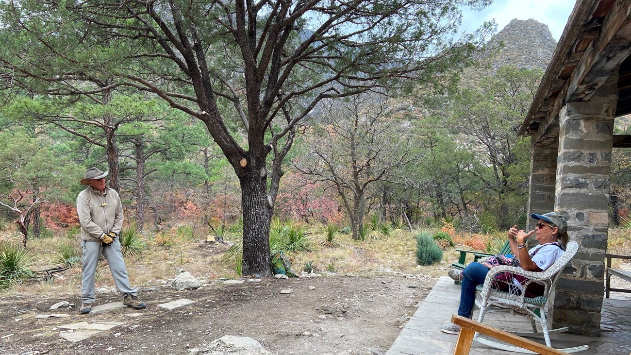 Volunteer speaks to a visitor seated on the porch of a stone cabin