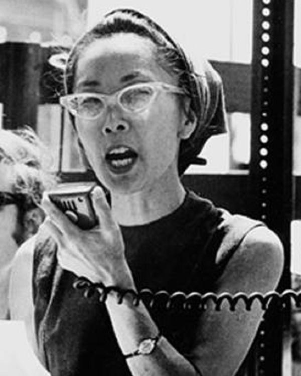 Asian woman with cat-eye glasses holding megaphone speaker.