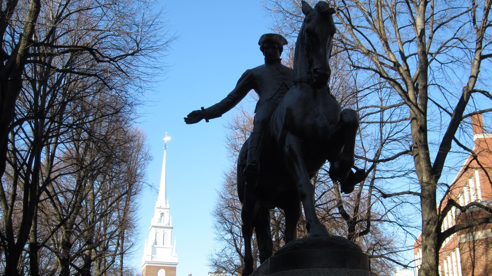 A bronze statue of Paul Revere riding a horse in front of the white steeple of Old North Church