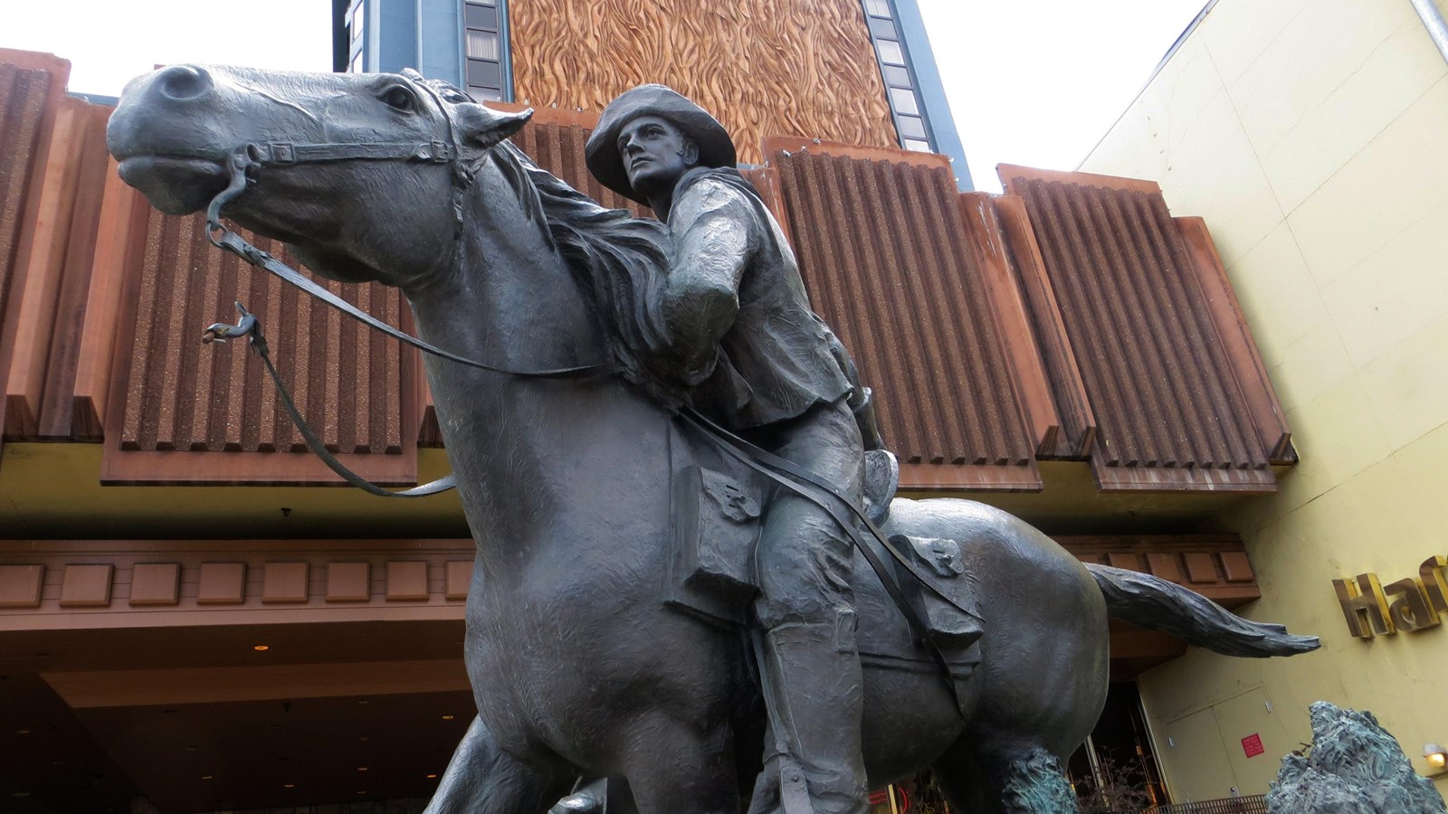 The view looks up at a bronze sculpture of a galloping horse and rider. A modern building behind.