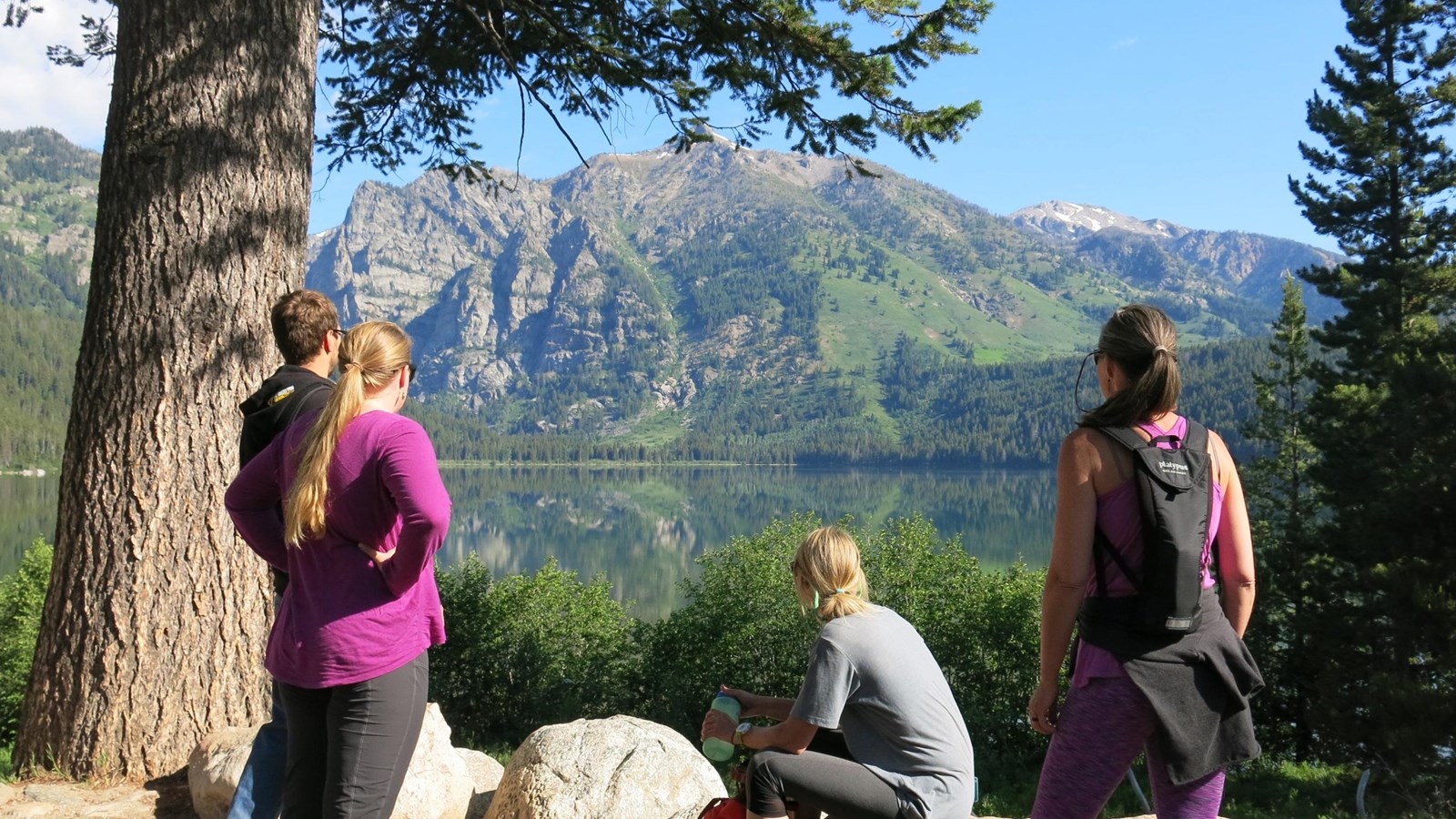 Hikers viewing a lake with mountains reflected into it.