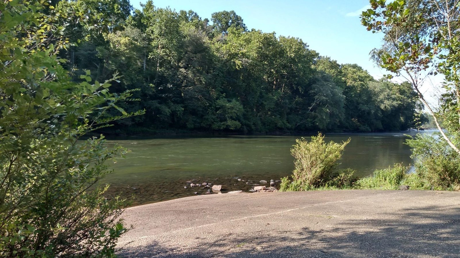 Concrete ramp in foreground leading to the river with a wooded shoreline in the distance.