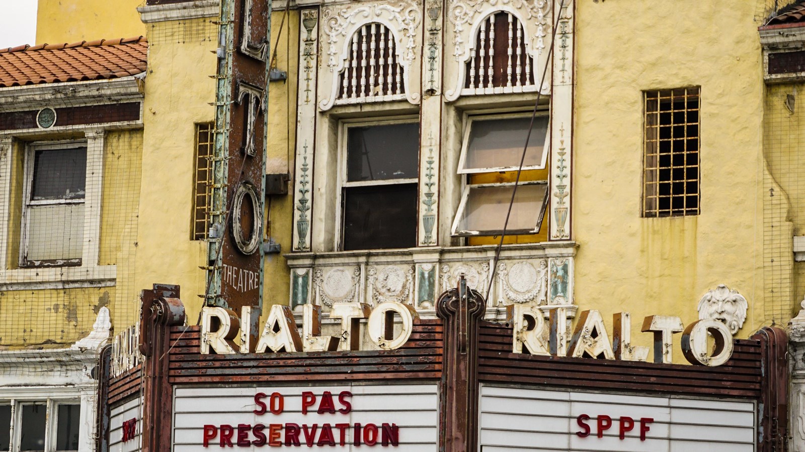 A large tan building with an ornate facade and a letter board that reads above