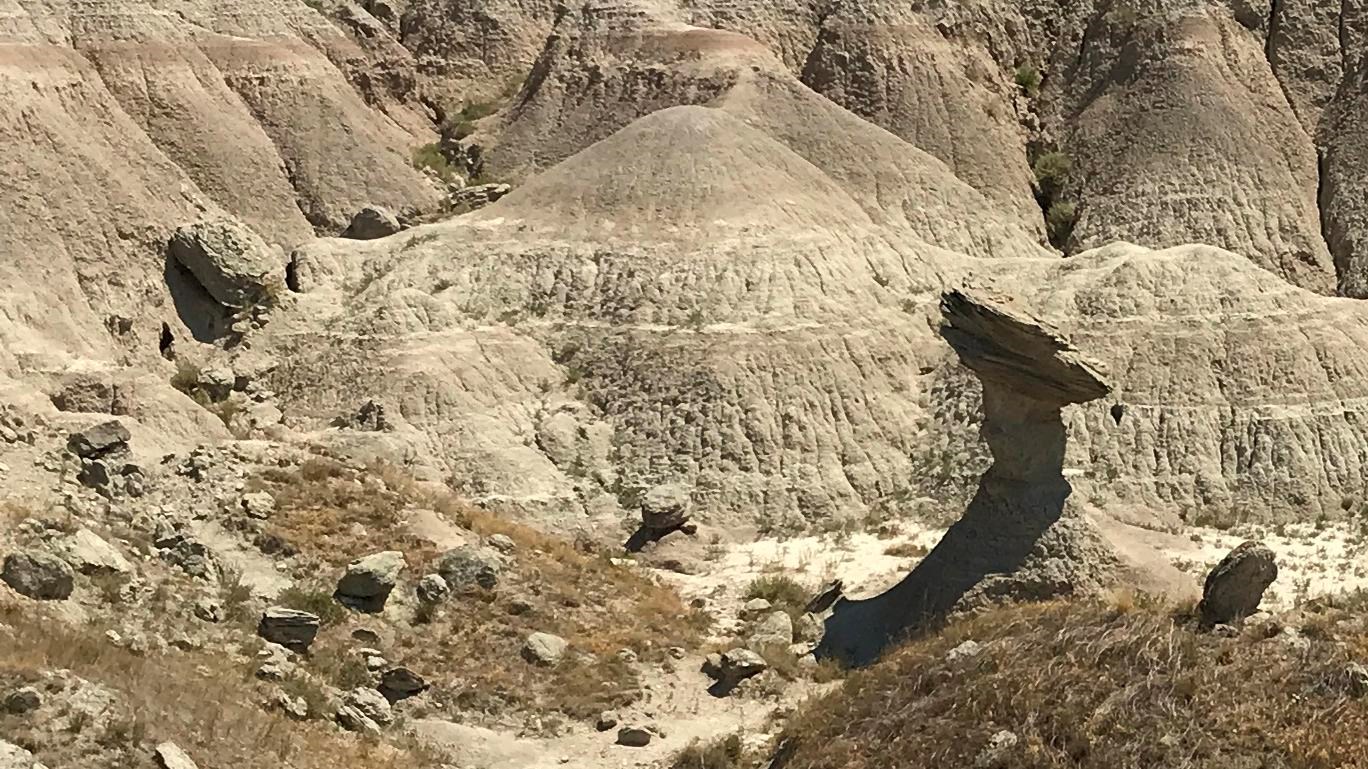 Nestled amid rolling badlands a rock lies sideways across a small pillar of dirt.