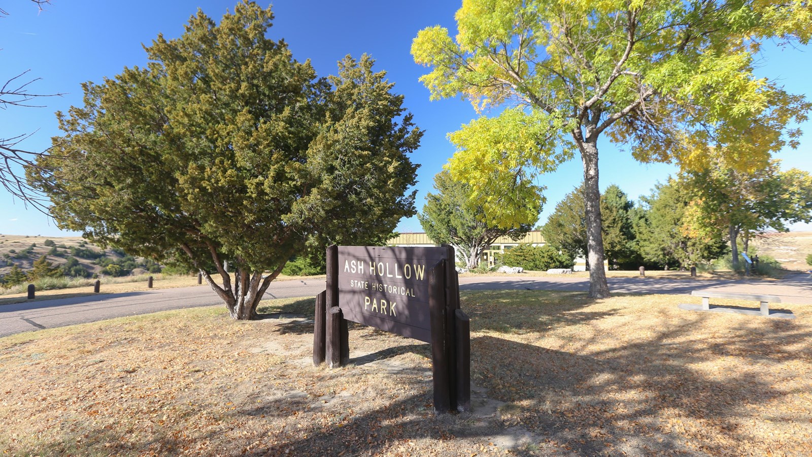 A brown entrance sign sits at the entrance to a grassy park with a trees.