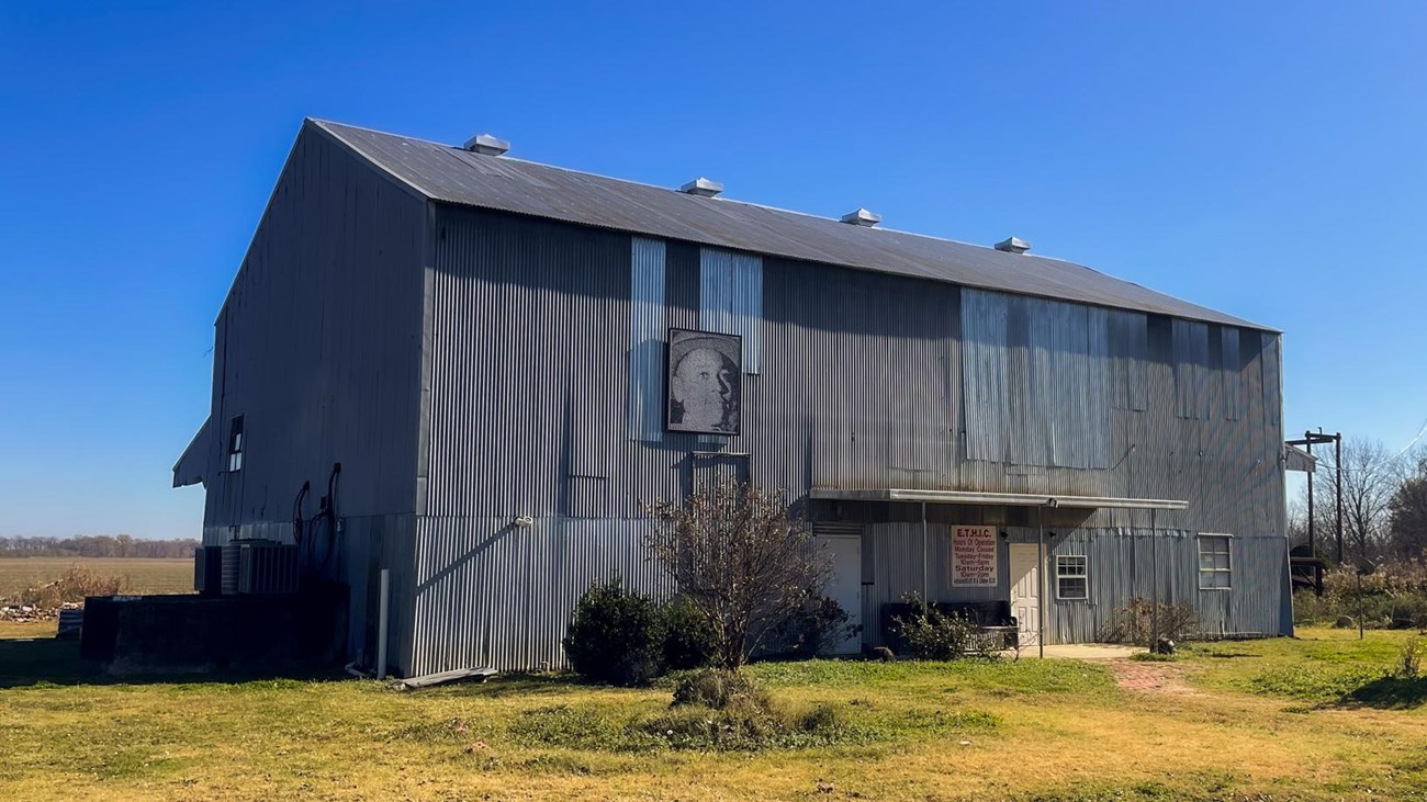 A metal cotton gin building sits in an open field