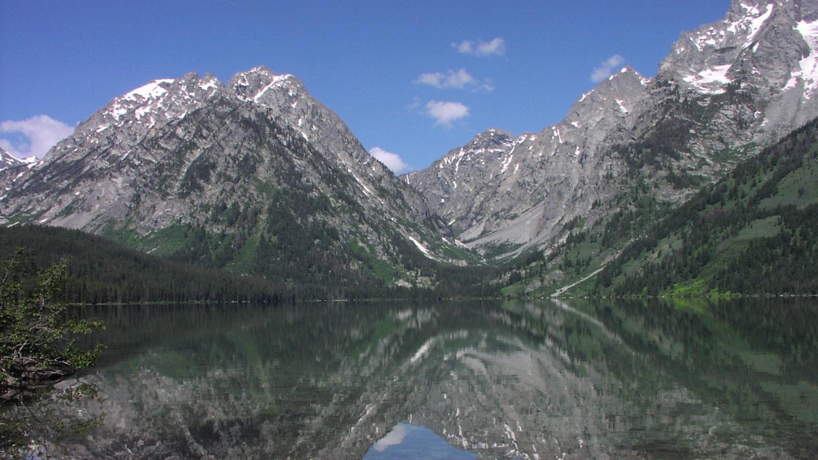 A lake mirrors the scene of mountains soaring to high elevations with a deep blue sky.