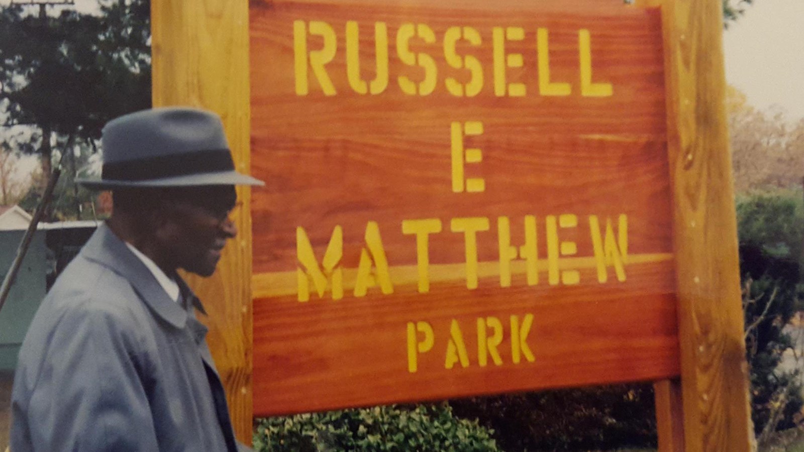 man with hat standing in front of park sign 
