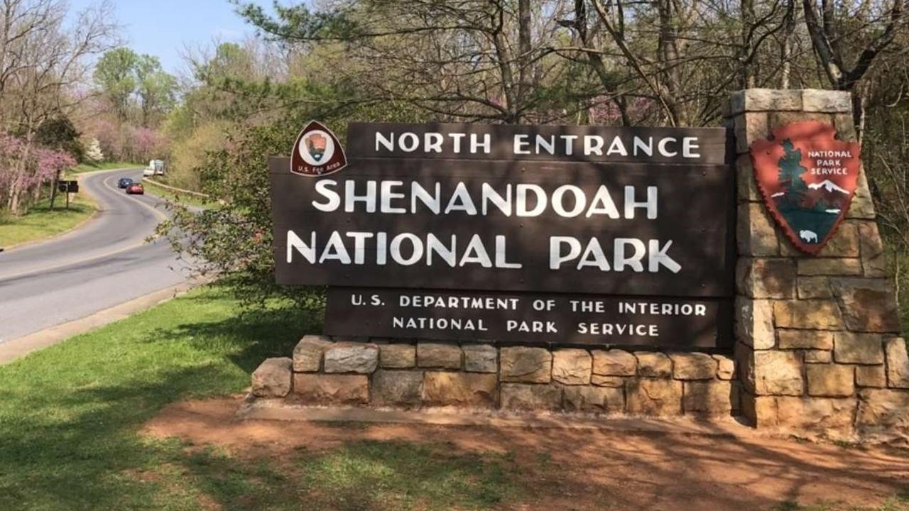 Sign to the left of a curving road for leading to the entrance station of Shenandoah National Park.