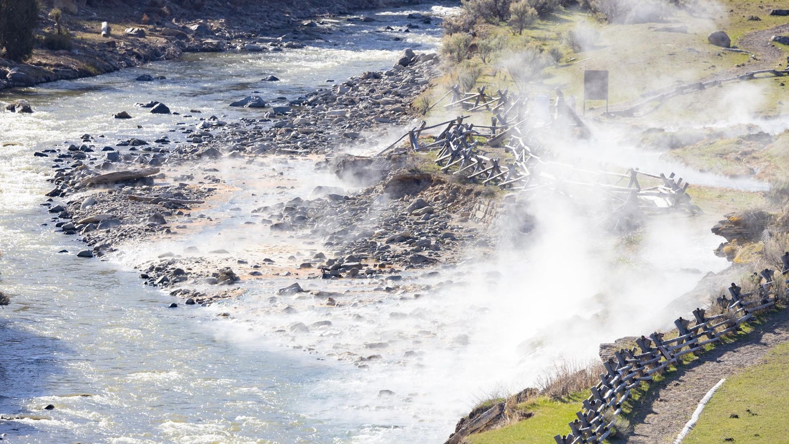 Steam rises from exposed rocks on a bank alongside a river.