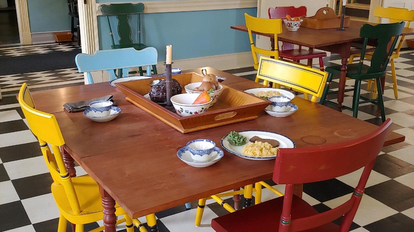 A black and white painted canvas floor with bright chairs at tables. There is reproduction food.