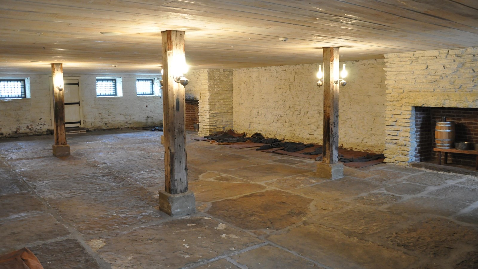 Large room with flagstone floor. Mats with blankets line the wall. Lamps attached to 4 posts.