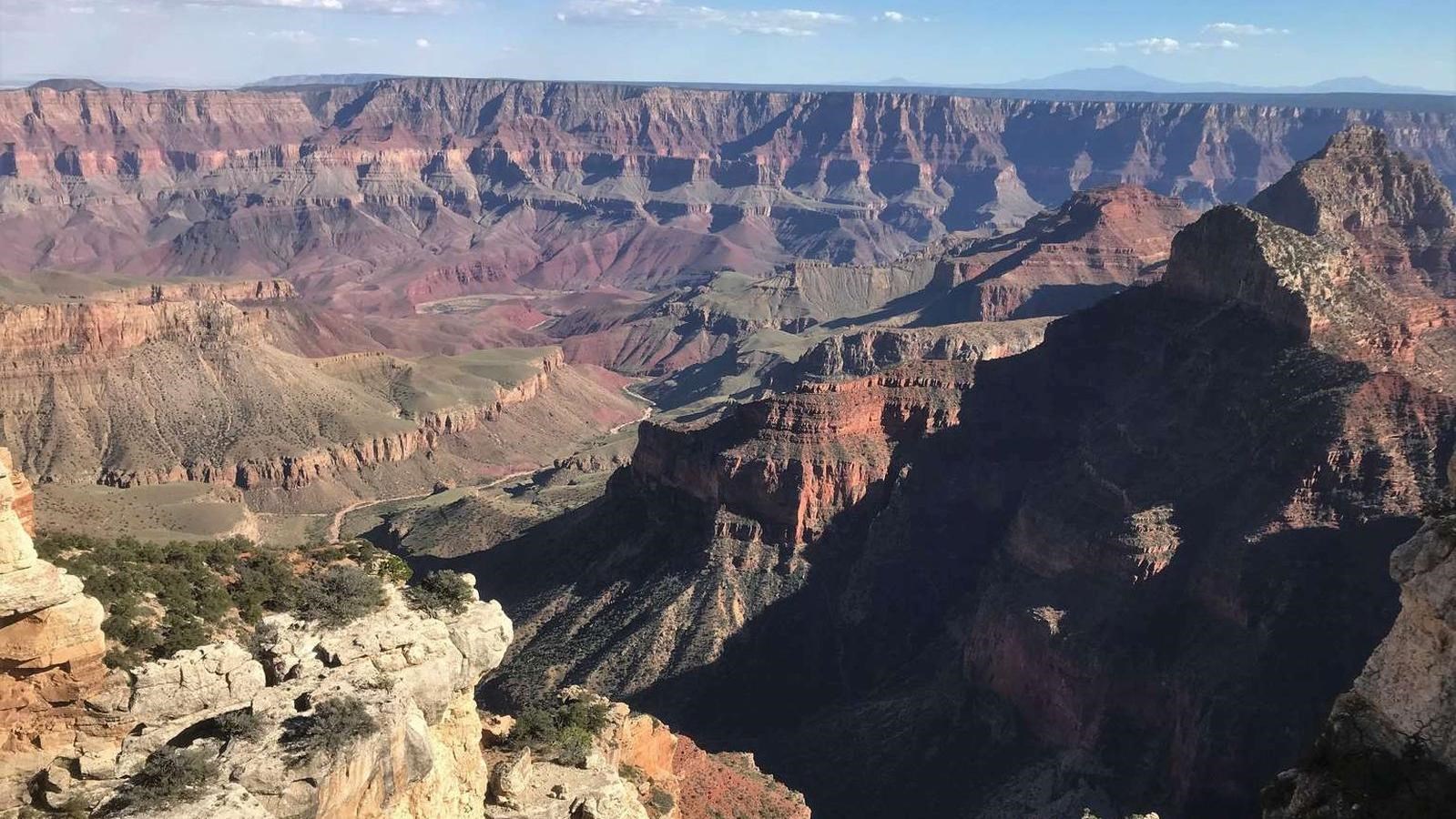 Steep cliffs are shadowed to the right as multicolored horizontal layers make up the Grand Canyon.