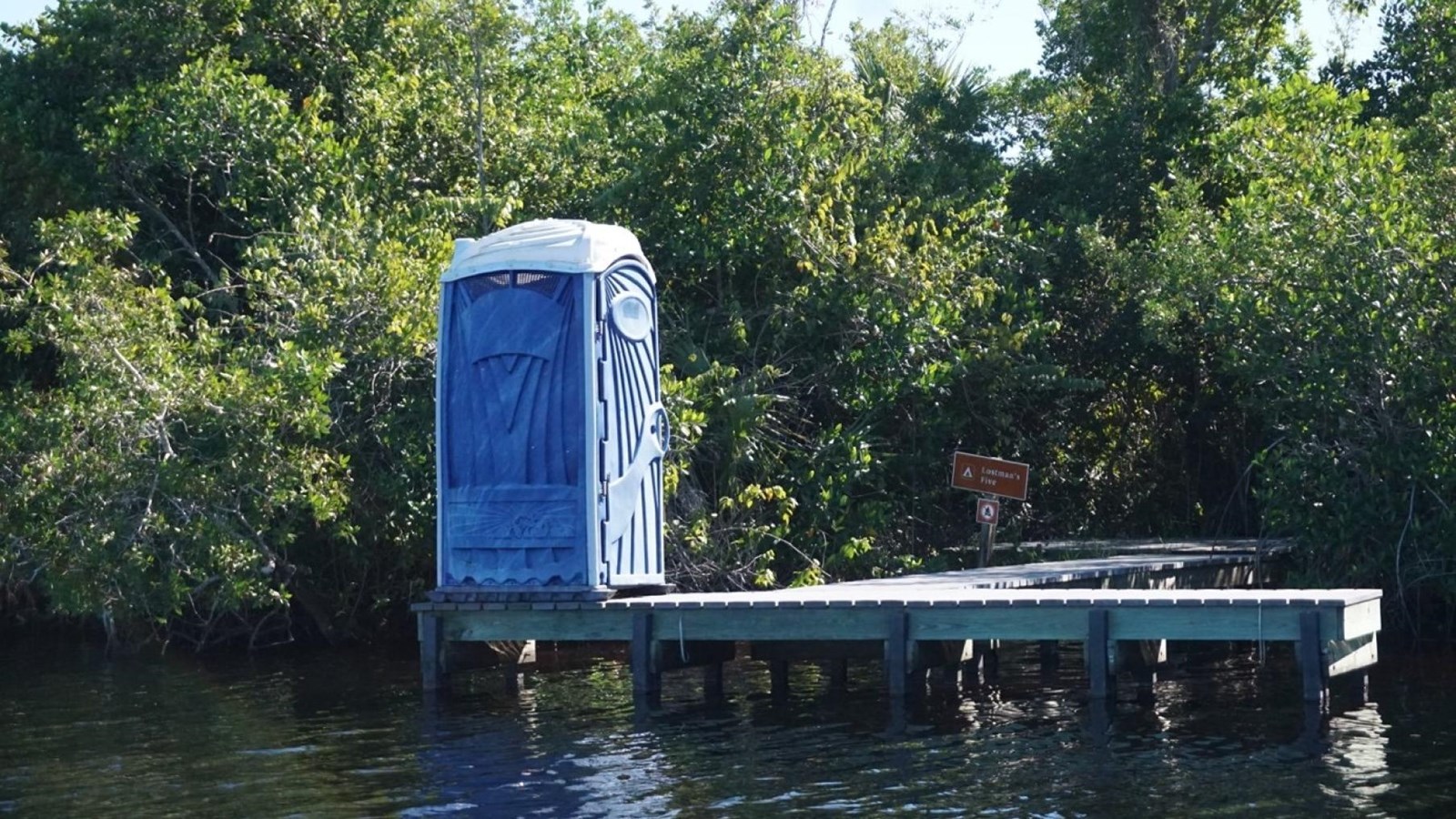 A small dock with a blue vault toilet. A clearing in the vegetation leads to camp clearing