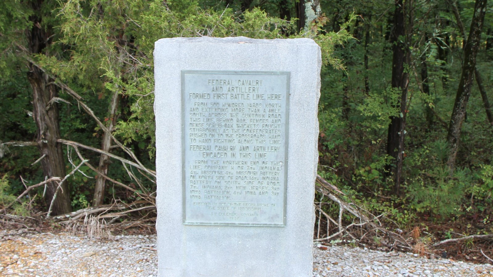 4 foot tall granite marker at edge of parking area. Thicket of trees behind marker. 