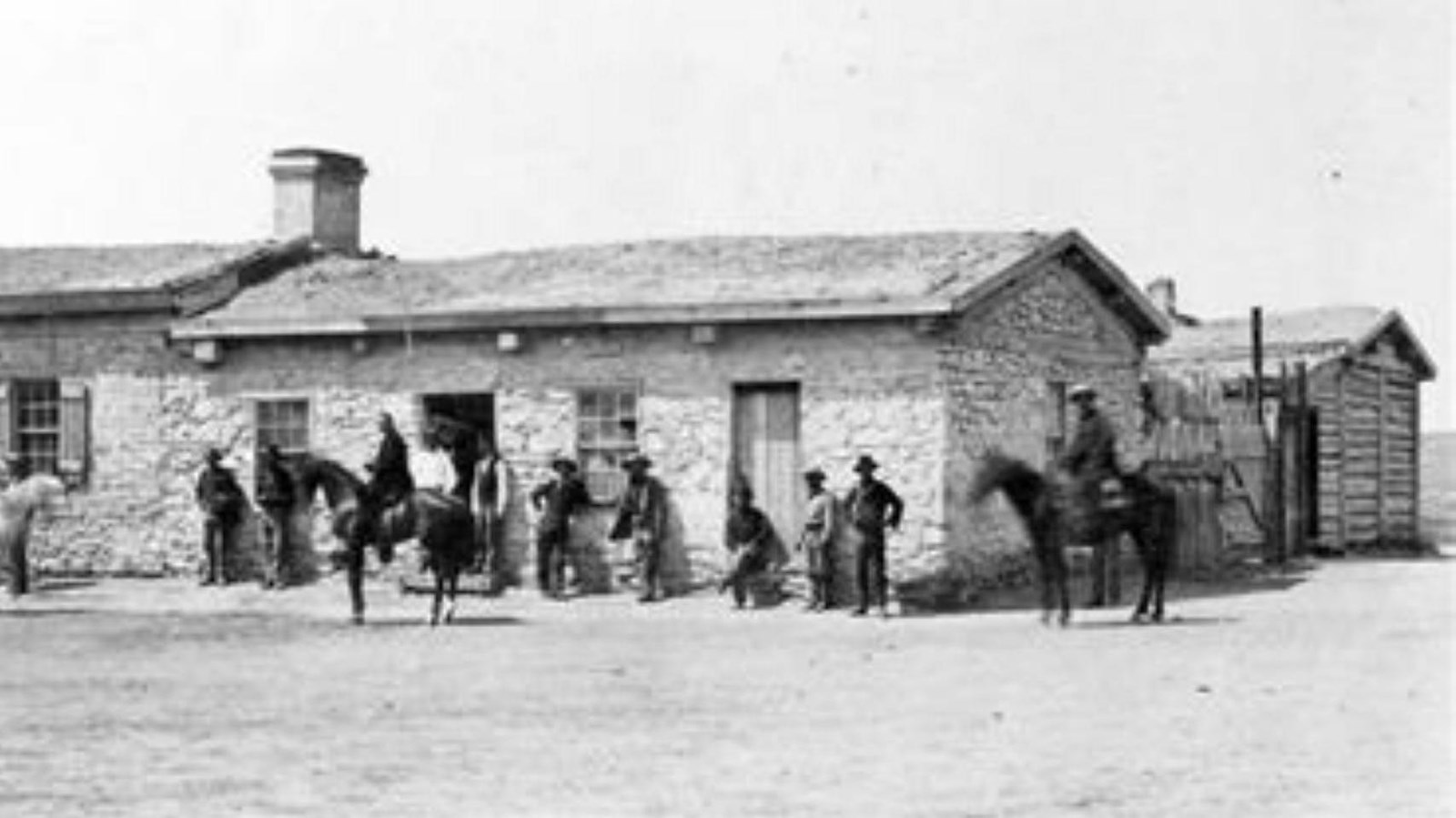 Several men stand in front of a lime grout colored building facing the camera.