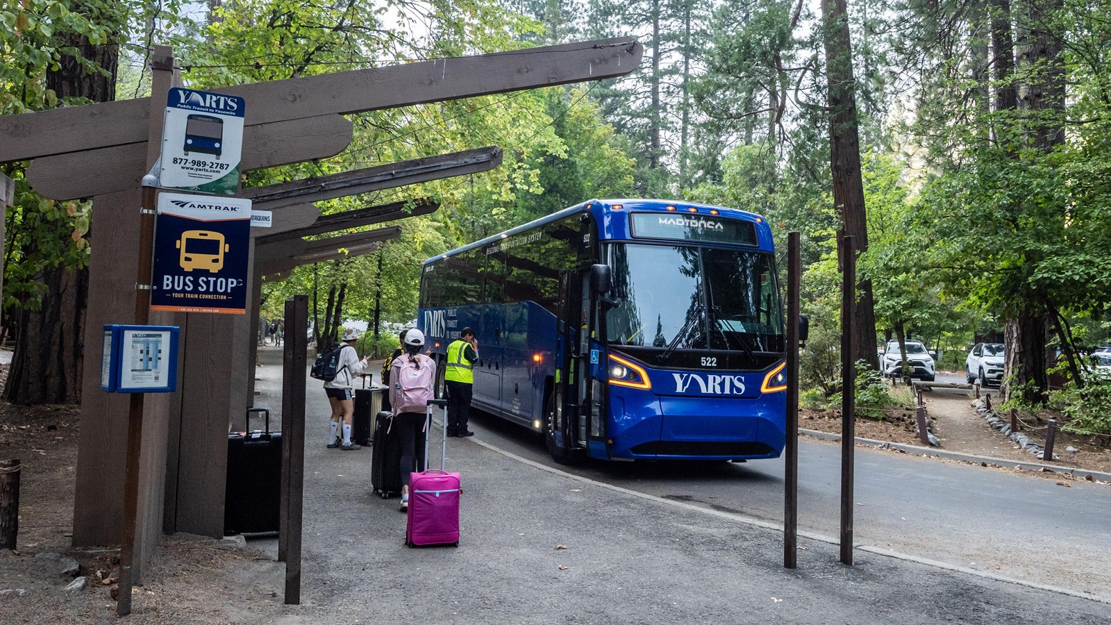 Passengers with suitcases board a large blue bus near signage reading