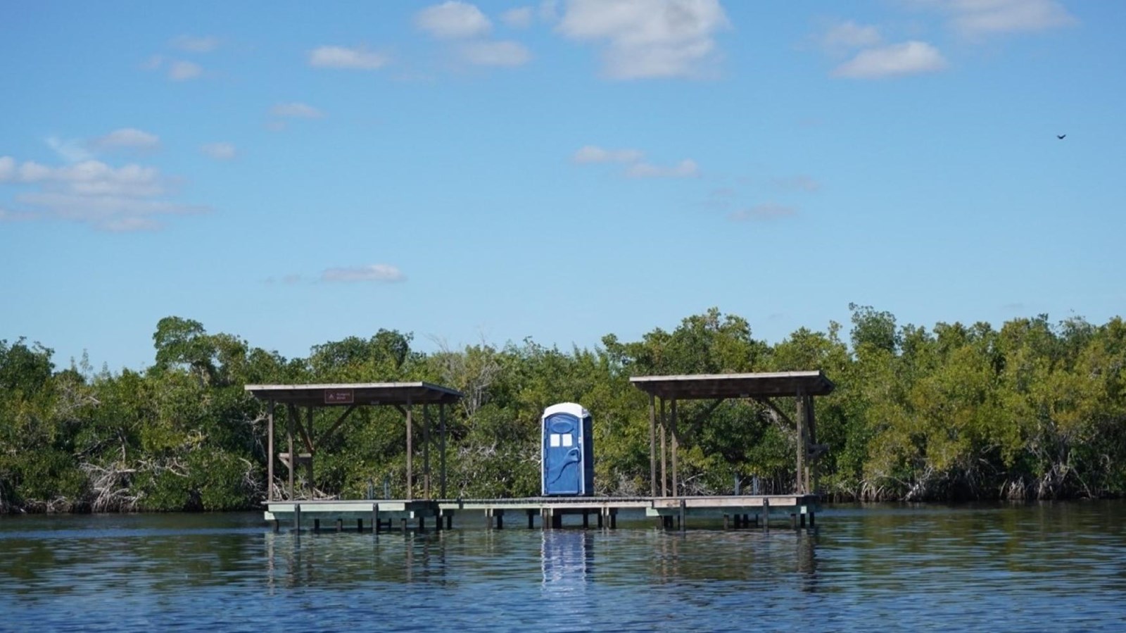 Two open air platforms over the water with two roofs. A blue vault toilet is in between them