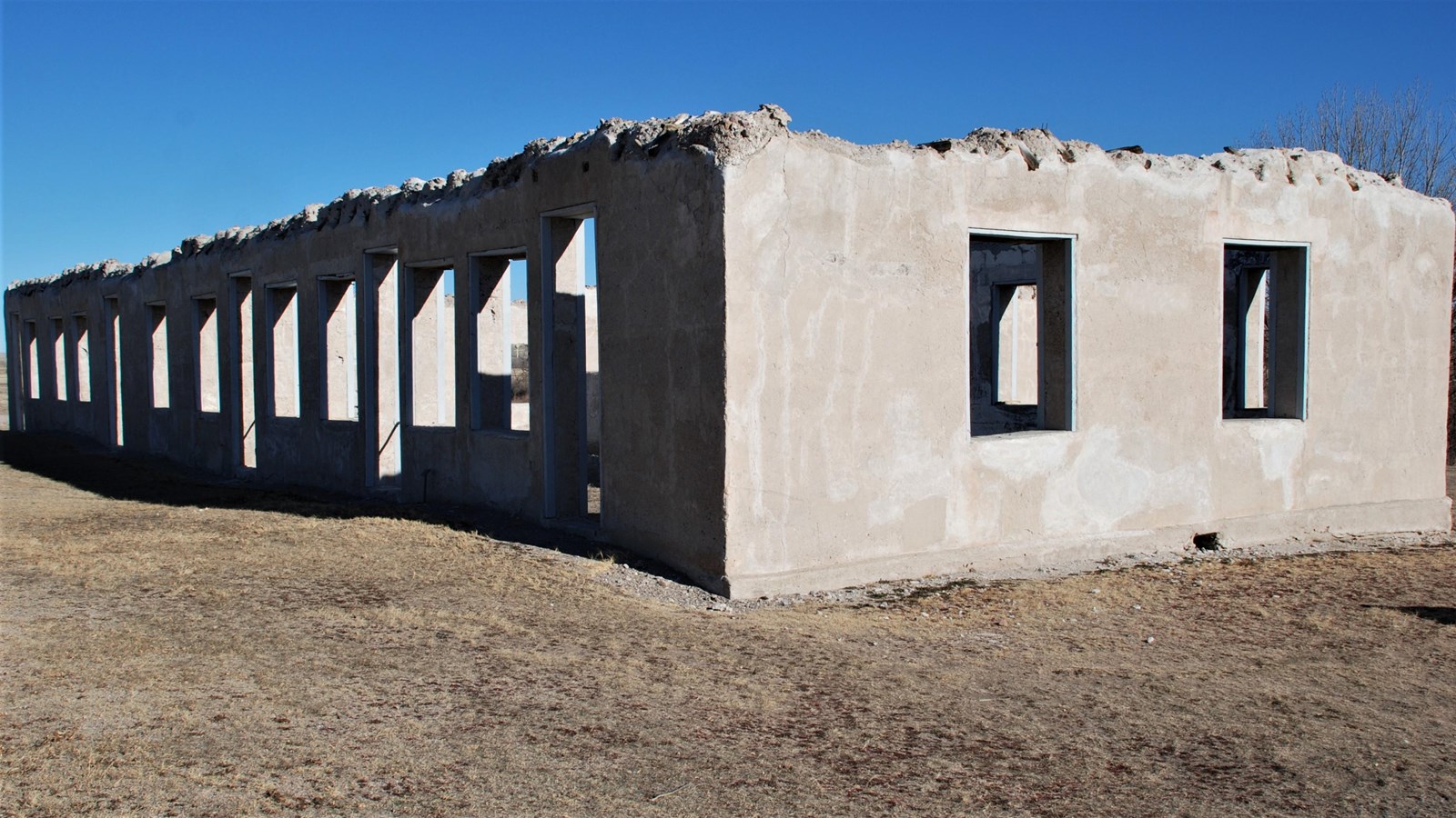 A rectangular lime-ground cement ruin without a roof and many empty windows and doorways.