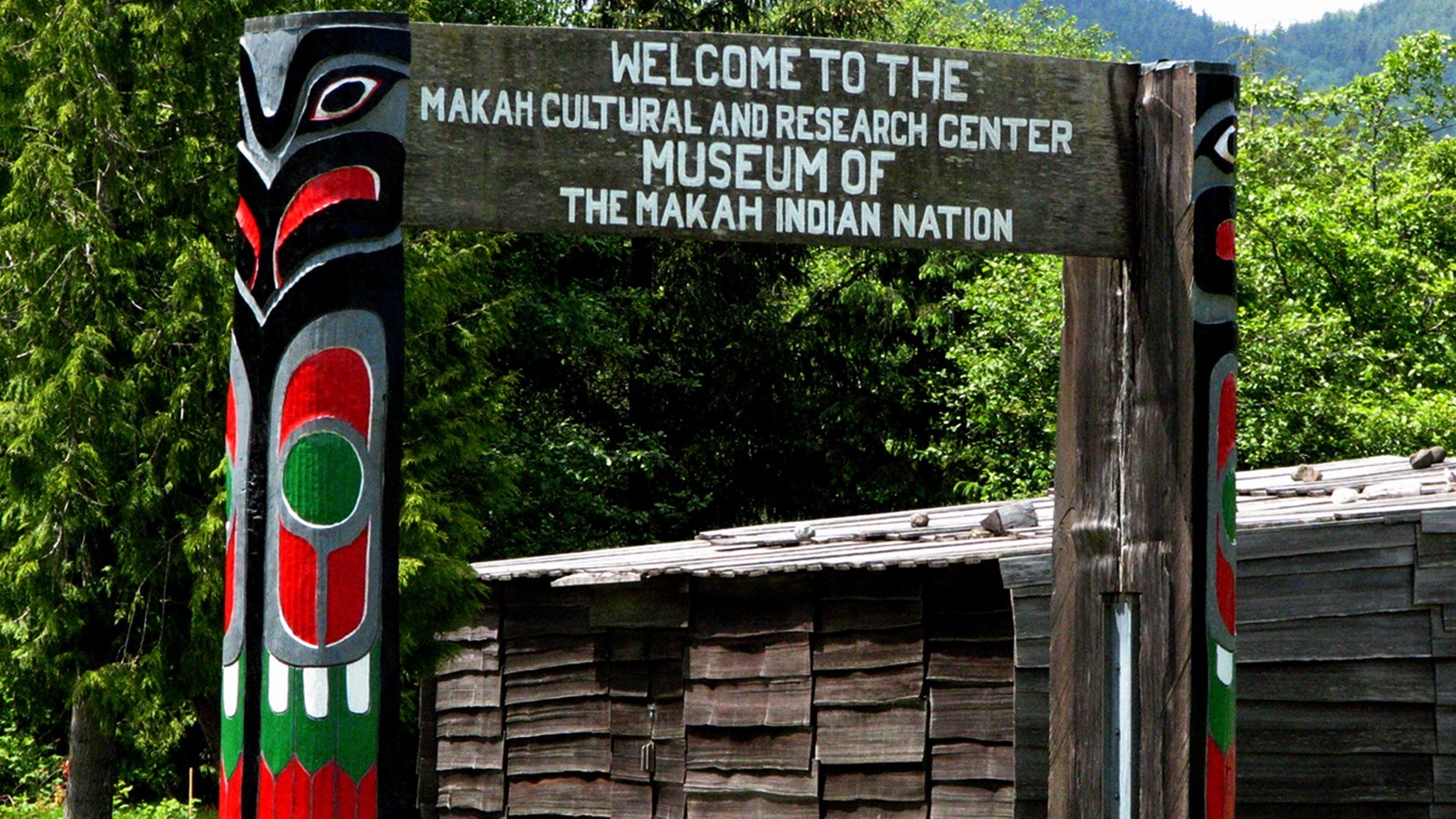 Two totem poles hold a sign that reads Welcome to the Makah Cultural and Research Center