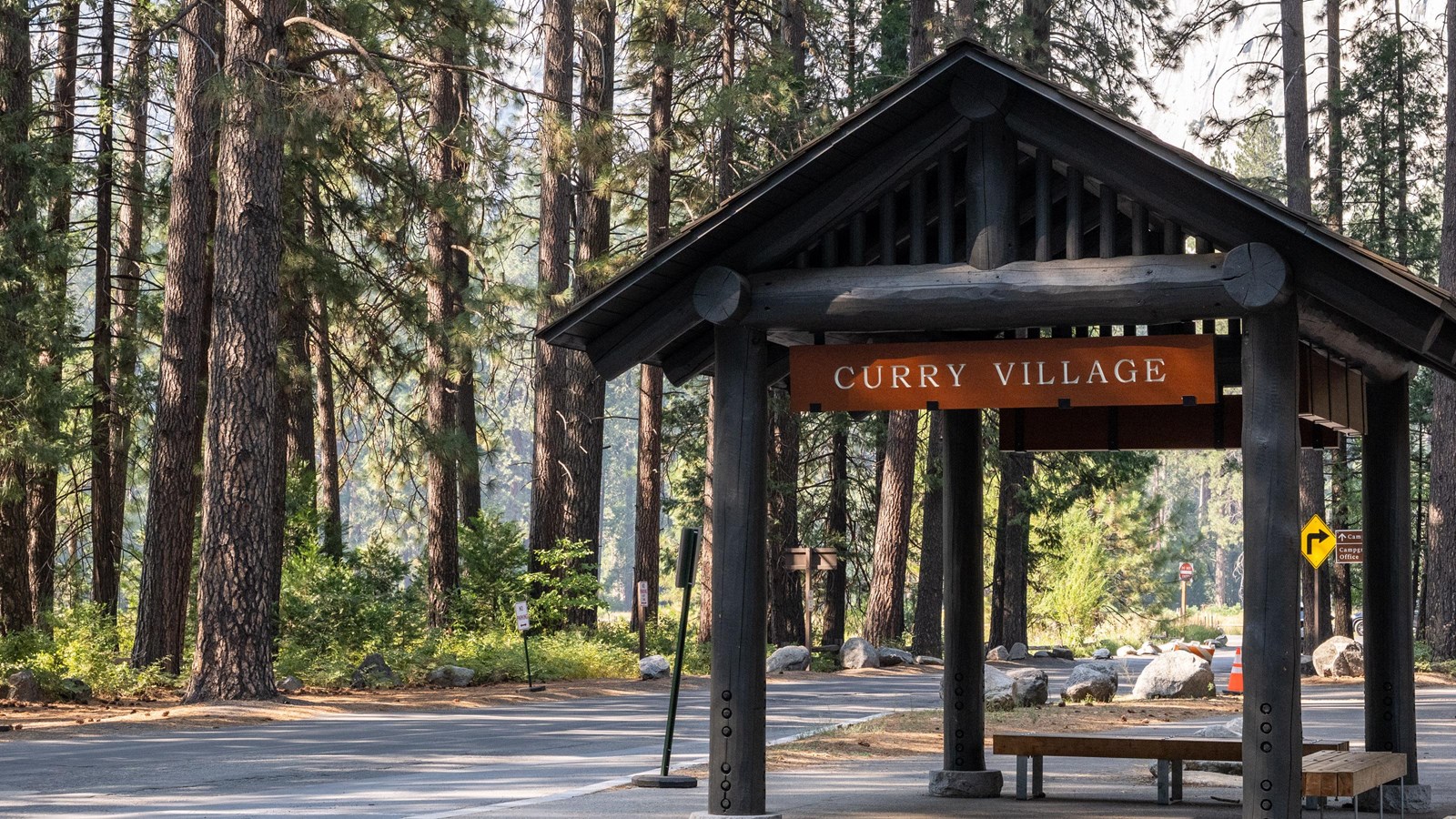 A covered wood shelter with several benches; a sign hanging above reads 