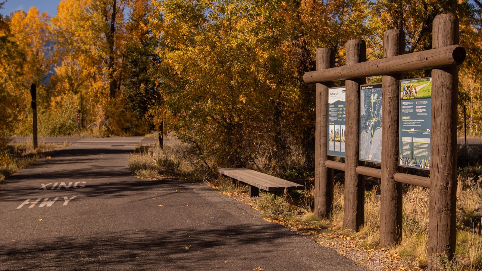 Three informational panels in a wooden frame next to a paved pathway heading away from the viewer.