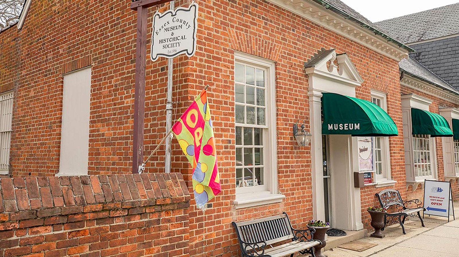 Brick building of the Essex County Museum with green awnings and open sign.