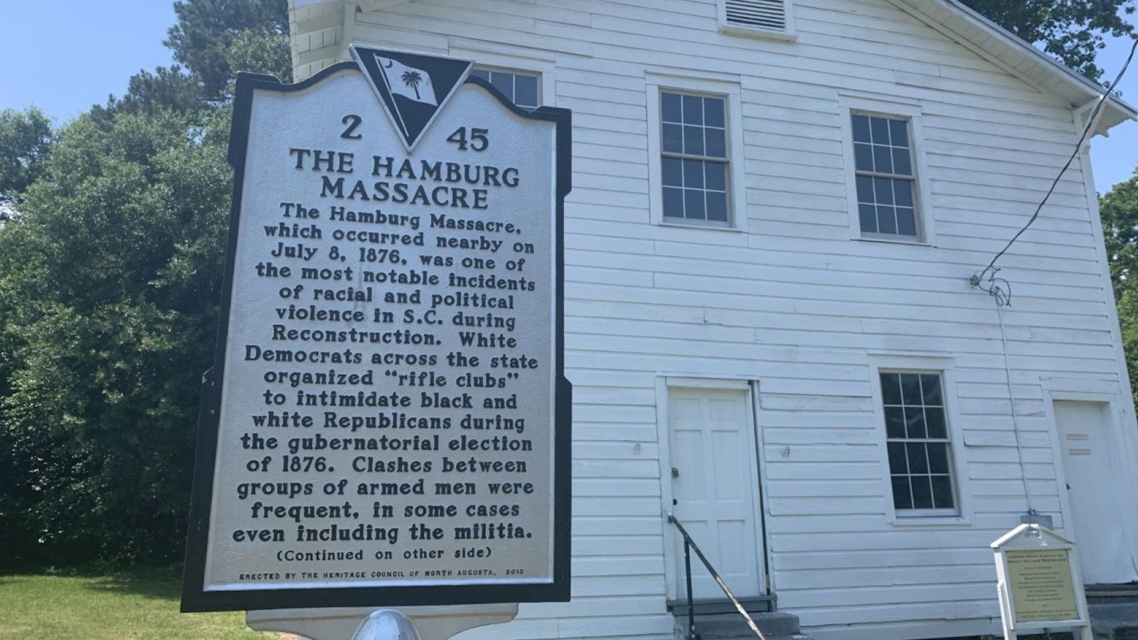 A white two-story building stands behind a white sign that reads 