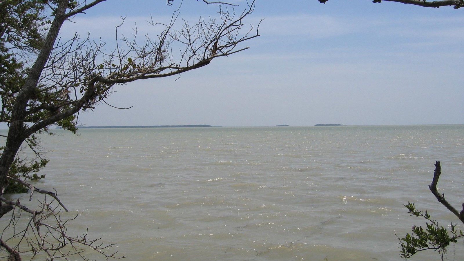 A break in the mangroves shows a view of blue/green Florida bay and green islands in the distance