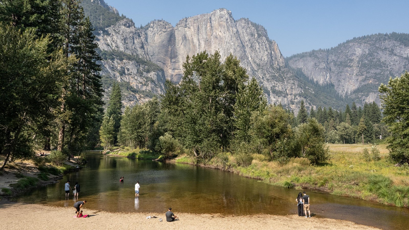 Visitors on the beach and in the water below a granite cliff with a dry waterfall
