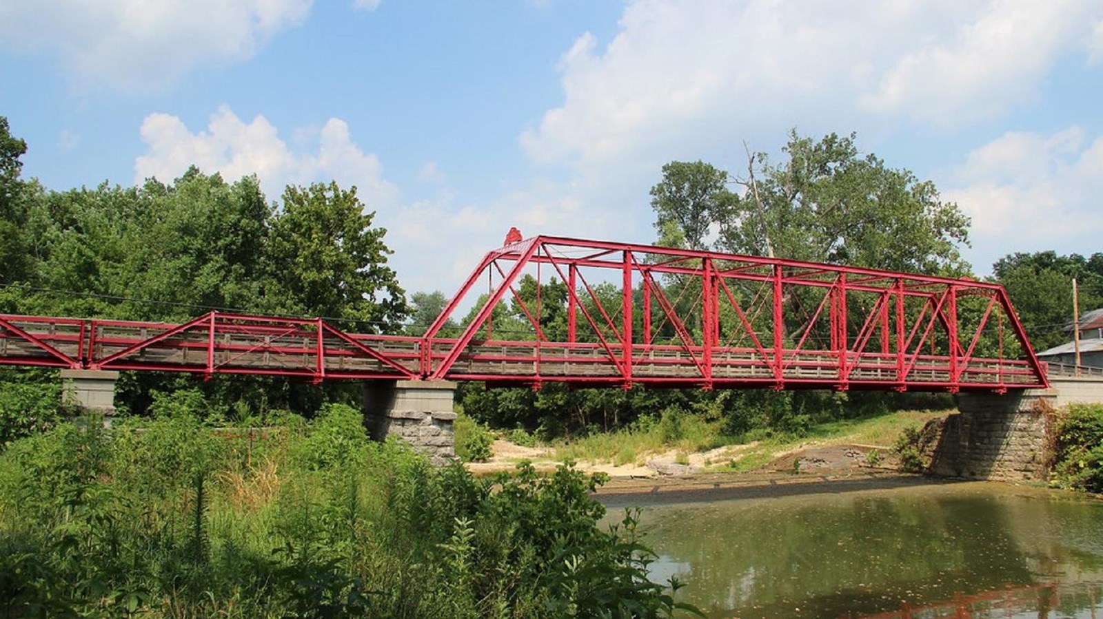 A red steel bridge spans a wide river lined with trees