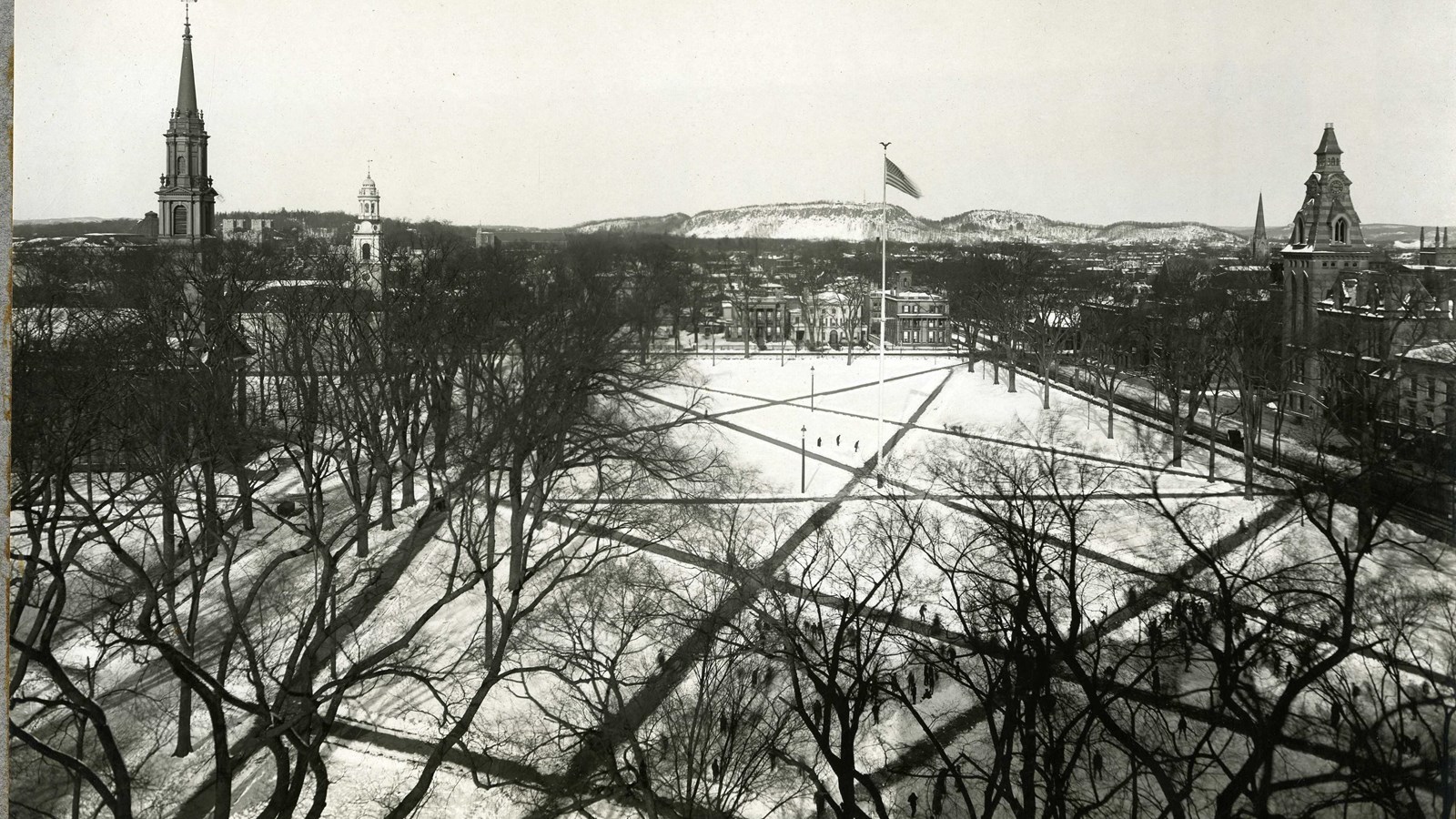 Black and white aerial of rectangular space between buildings with straight lines crossing grass
