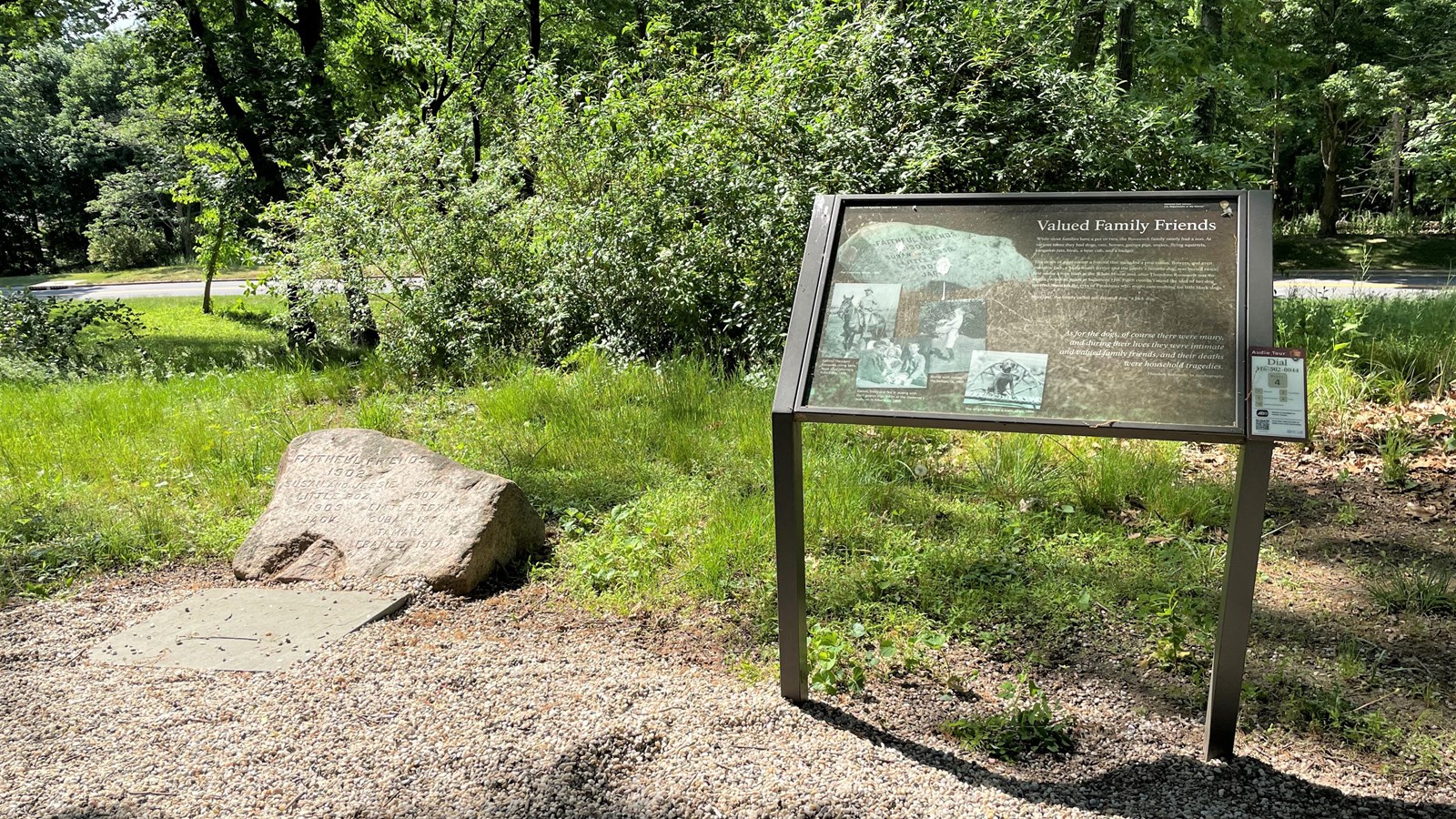 An large engraved stone sits near a metal sign at the edge of a grassy area.
