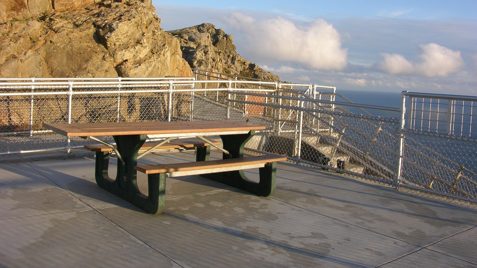 A picnic table in the middle of a paved observation deck with a view looking out across the ocean.